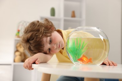 Photo of Little boy with goldfish in aquarium on table at home