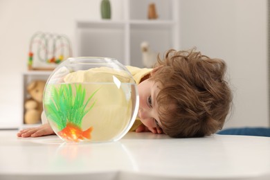 Photo of Little boy with goldfish in aquarium on table at home