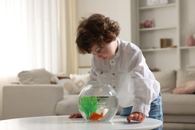 Photo of Little boy with goldfish in aquarium on table at home