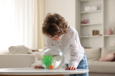 Photo of Little boy with goldfish in aquarium on table at home