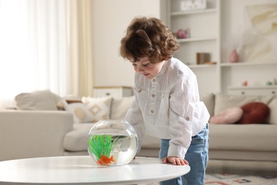 Photo of Little boy with goldfish in aquarium on table at home