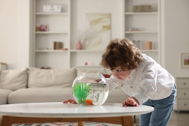 Photo of Little boy with goldfish in aquarium on table at home. Space for text