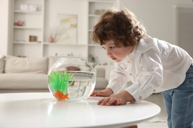 Photo of Little boy with goldfish in aquarium on table at home