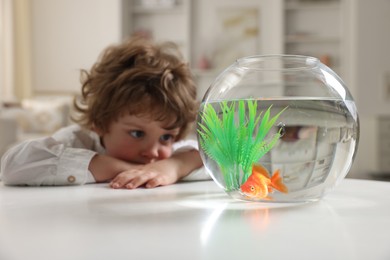 Photo of Little boy with goldfish in aquarium on table at home