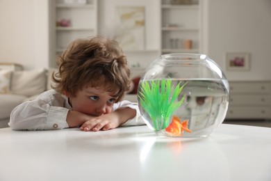 Photo of Little boy with goldfish in aquarium on table at home