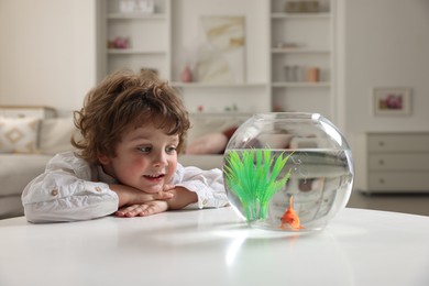 Photo of Little boy with goldfish in aquarium on table at home