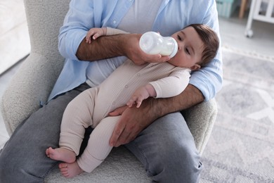 Photo of Father feeding his little baby with bottle on armchair at home, closeup