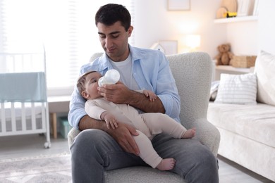 Photo of Father feeding his little baby with bottle on armchair at home