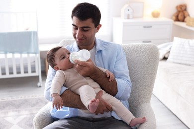 Photo of Father feeding his little baby with bottle on armchair at home