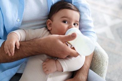 Photo of Father feeding his little baby with bottle on armchair at home, closeup