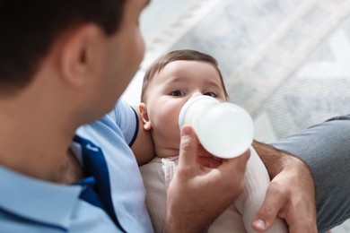 Photo of Father feeding his little baby with bottle on sofa at home, closeup
