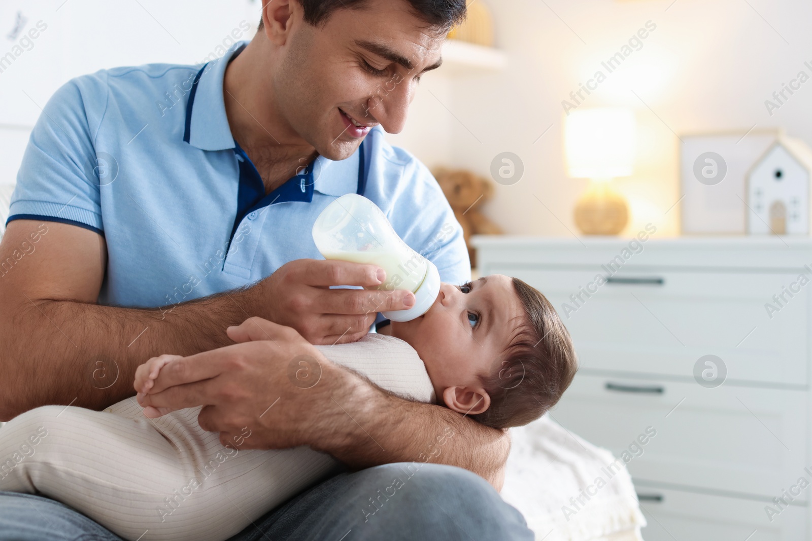 Photo of Father feeding his little baby with bottle on sofa at home, closeup