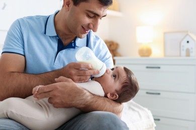 Photo of Father feeding his little baby with bottle on sofa at home, closeup