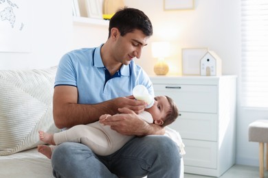 Photo of Father feeding his little baby with bottle on sofa at home. Space for text
