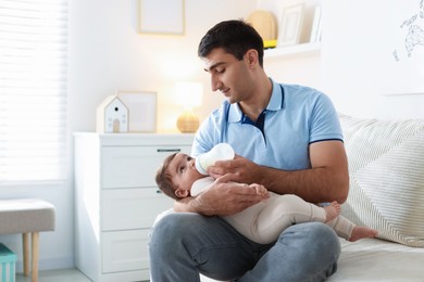 Photo of Father feeding his little baby with bottle on sofa at home. Space for text