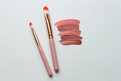 Photo of Colorful lip glosses and makeup brushes on grey background, flat lay