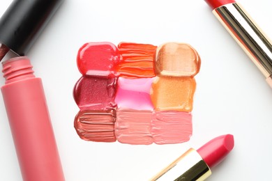Photo of Colorful lip glosses and lipsticks on white background, flat lay