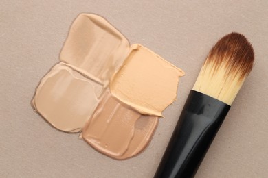 Photo of Colorful skin foundations and makeup brush on grey background, flat lay