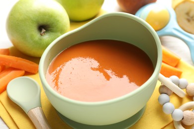 Photo of Baby food. Tasty puree in bowl, different ingredients and teether on table, closeup