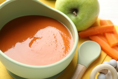Photo of Baby food. Tasty puree in bowl, different ingredients and teether on table, closeup