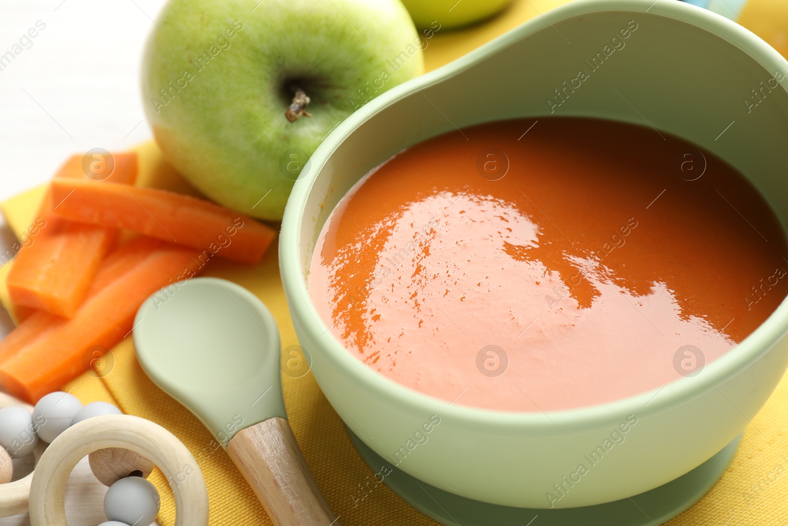 Baby food. Tasty puree in bowl, different ingredients and teether on table, closeup Photo of Baby food. Tasty puree in bowl, different ingredients and teether on table, closeup