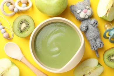Photo of Baby food. Tasty puree in bowls, different ingredients and toys on yellow background, flat lay