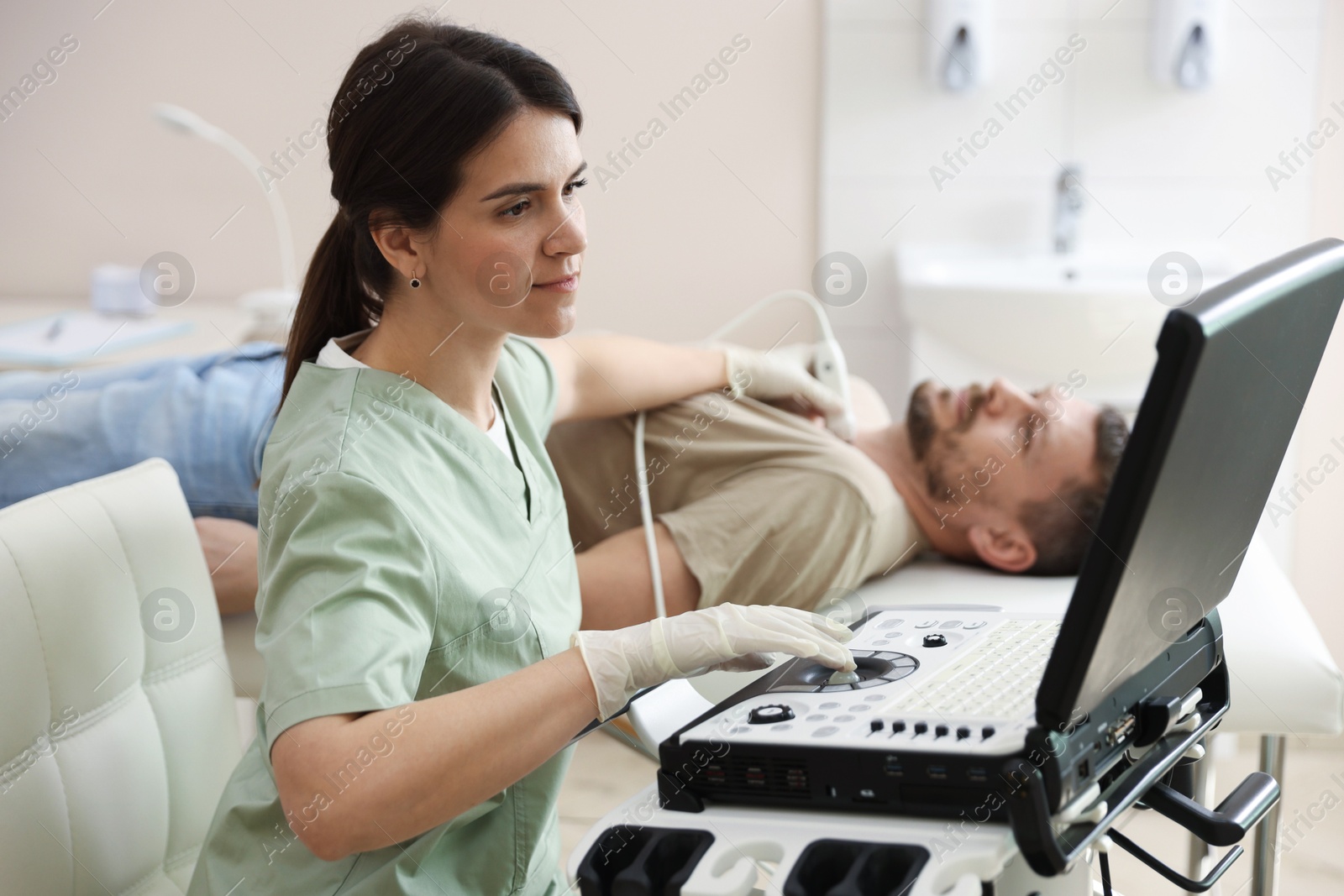 Photo of Sonographer conducting ultrasound examination of man's thyroid gland in clinic