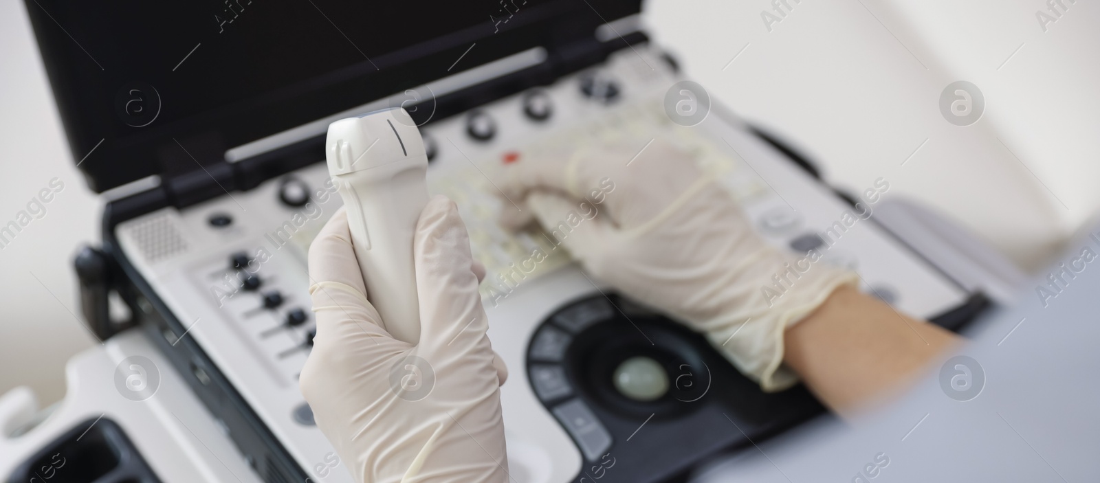 Photo of Sonographer with transducer and ultrasound machine in clinic, closeup