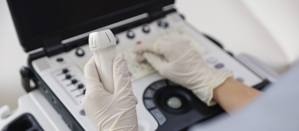 Photo of Sonographer with transducer and ultrasound machine in clinic, closeup