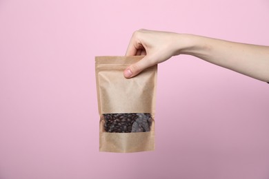 Photo of Woman holding zipper stand-up pouch with coffee beans on pink background, closeup. Mockup for design