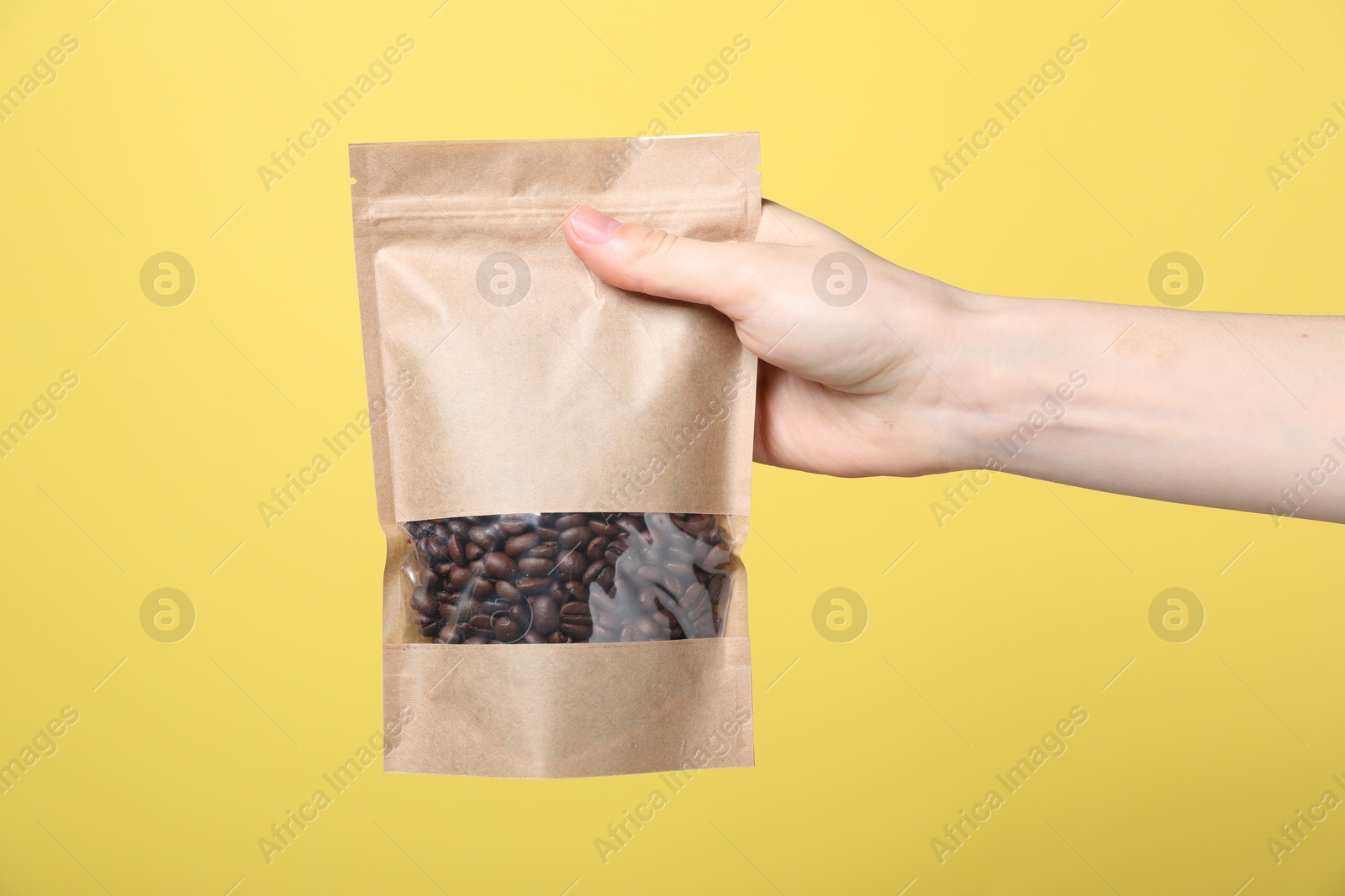 Woman holding zipper stand-up pouch with coffee beans on yellow background, closeup. Mockup for design Photo of Woman holding zipper stand-up pouch with coffee beans on yellow background, closeup. Mockup for design