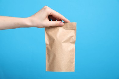 Photo of Woman with zipper stand-up pouch on light blue background, closeup. Mockup for design