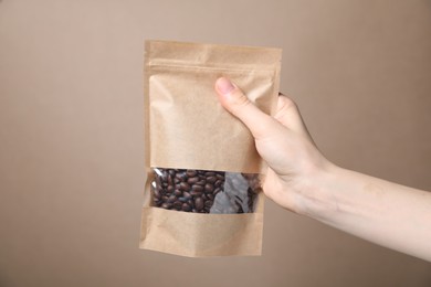 Photo of Woman holding zipper stand-up pouch with coffee beans on beige background, closeup. Mockup for design