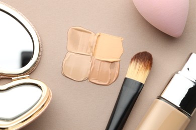 Photo of Colorful skin foundations and makeup brush on grey background, flat lay