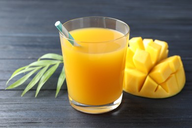 Photo of Tasty mango juice in glass, fresh fruit and green leaves on wooden table, closeup