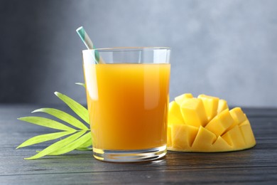 Photo of Tasty mango juice in glass, fresh fruit and green leaves on wooden table, closeup