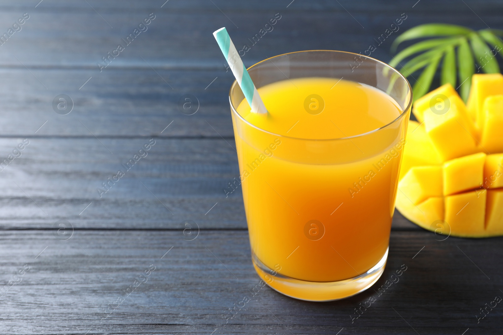 Tasty mango juice in glass, fresh fruit and green leaves on wooden table, closeup. Space for text Photo of Tasty mango juice in glass, fresh fruit and green leaves on wooden table, closeup. Space for text