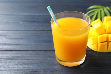 Photo of Tasty mango juice in glass, fresh fruit and green leaves on wooden table, closeup. Space for text