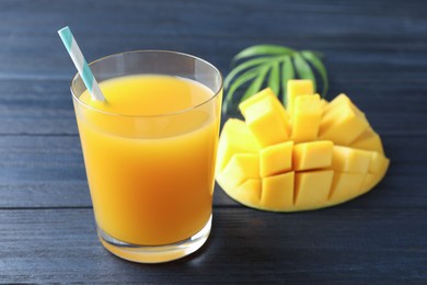 Photo of Tasty mango juice in glass, fresh fruit and green leaves on wooden table, closeup