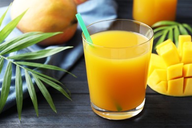 Photo of Tasty mango juice in glass, fresh fruits and green leaves on wooden table, closeup