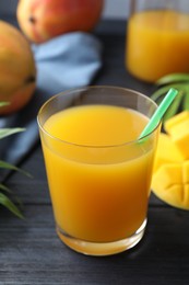 Photo of Tasty mango juice in glass, fresh fruits and green leaves on wooden table, closeup