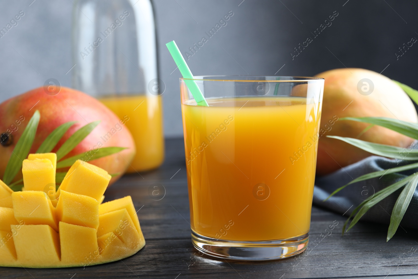 Tasty mango juice in glass, fresh fruits and green leaves on wooden table, closeup Photo of Tasty mango juice in glass, fresh fruits and green leaves on wooden table, closeup