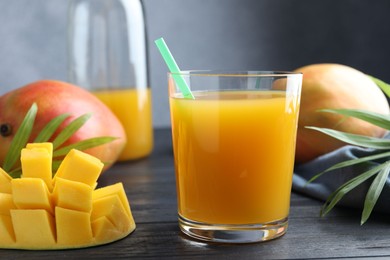 Photo of Tasty mango juice in glass, fresh fruits and green leaves on wooden table, closeup