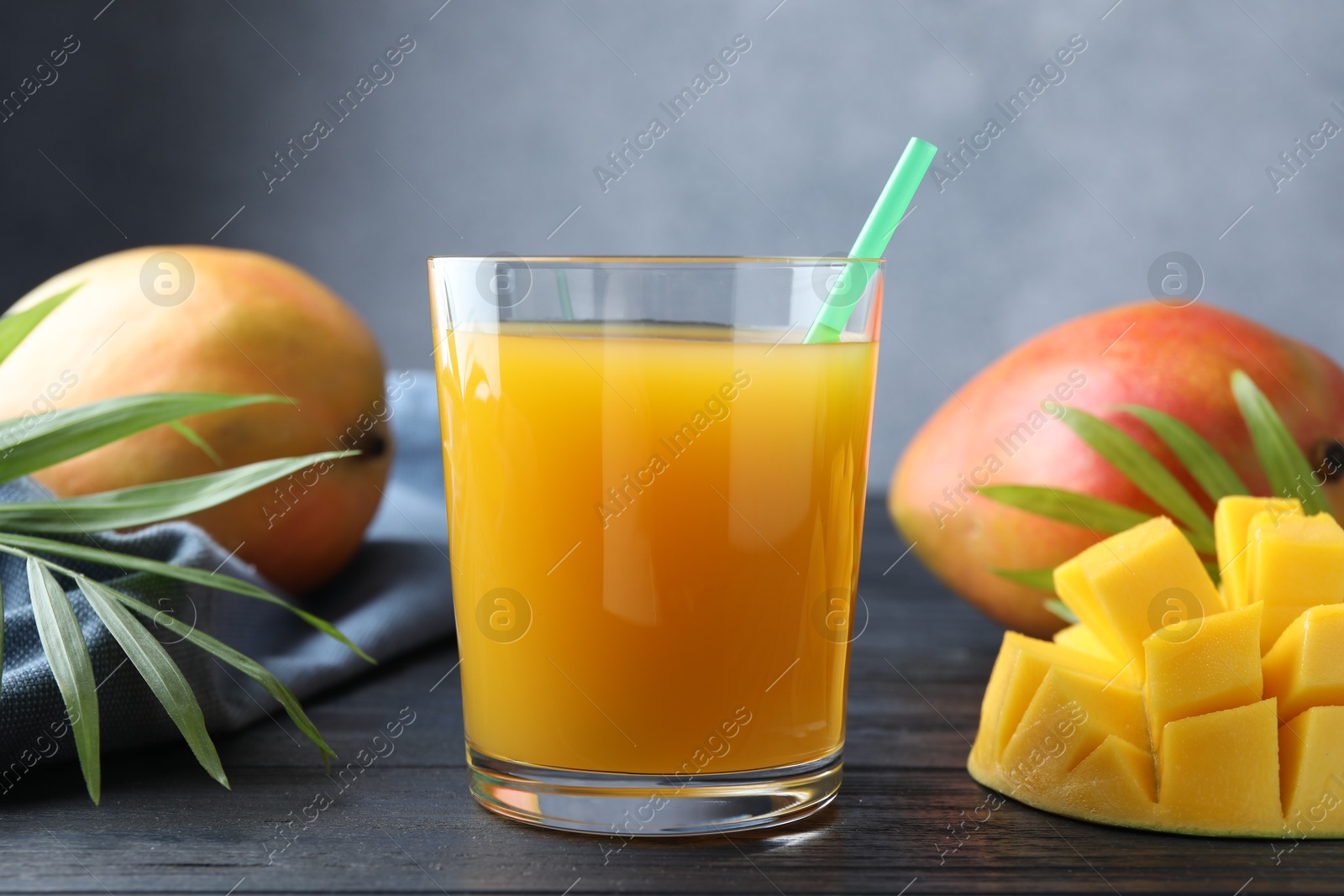 Tasty mango juice in glass, fresh fruits and green leaves on wooden table, closeup Photo of Tasty mango juice in glass, fresh fruits and green leaves on wooden table, closeup