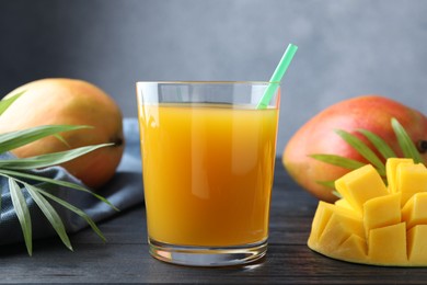 Photo of Tasty mango juice in glass, fresh fruits and green leaves on wooden table, closeup
