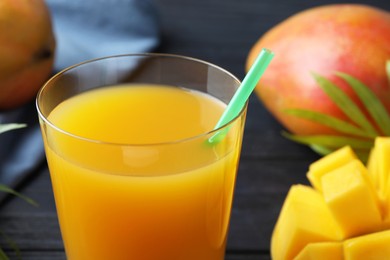 Photo of Tasty mango juice in glass, fresh fruits and green leaves on table, closeup