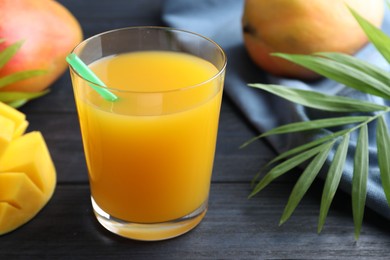 Photo of Tasty mango juice in glass, fresh fruits and green leaves on wooden table, closeup