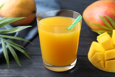 Photo of Tasty mango juice in glass, fresh fruits and green leaves on wooden table, closeup