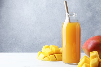 Photo of Tasty mango juice in glass bottle and fresh fruits on white table, space for text