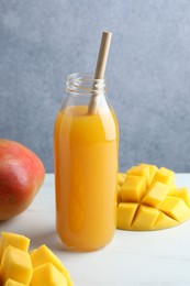 Photo of Tasty mango juice in glass bottle and fresh fruits on white table